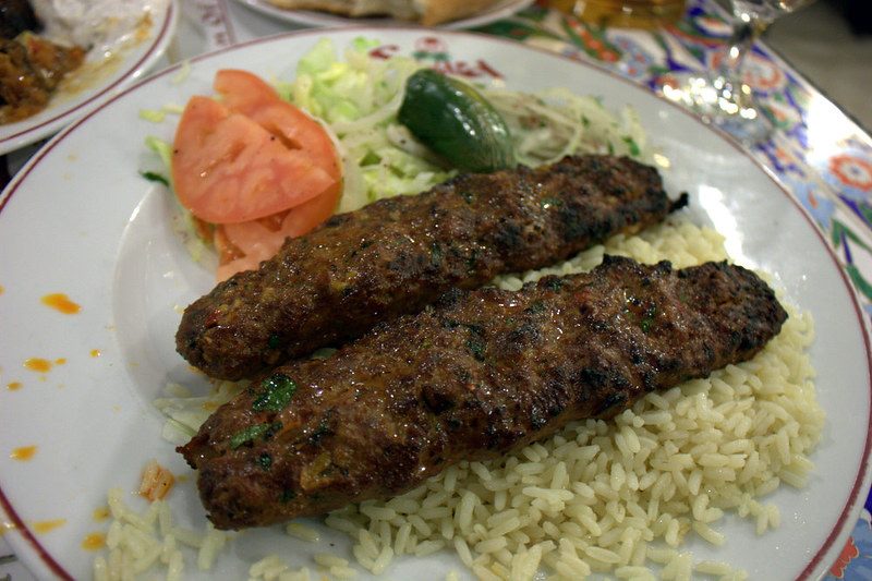 Two beef kebabs on a bed of rice, with tomatoes and salad on the side.