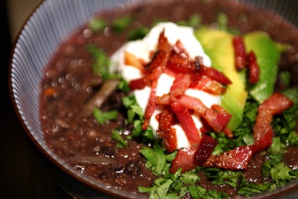 A bowl of black bean soup, topped with cilantro, sour cream, avocado, and roasted peppers.