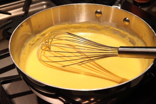 A pot of cheese sauce in a pot on the stove top.