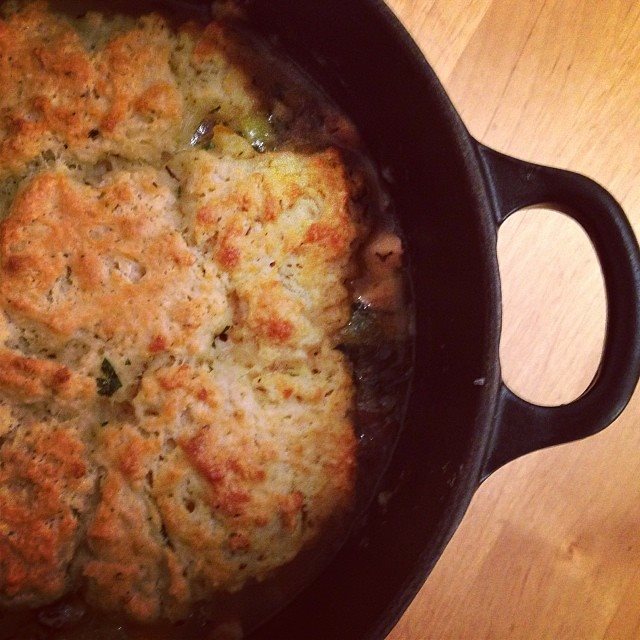 A cast iron pan filled with chicken pot pie, topped with biscuit.