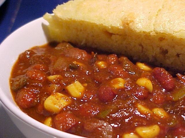 A bowl of chili with cornbread on the side.