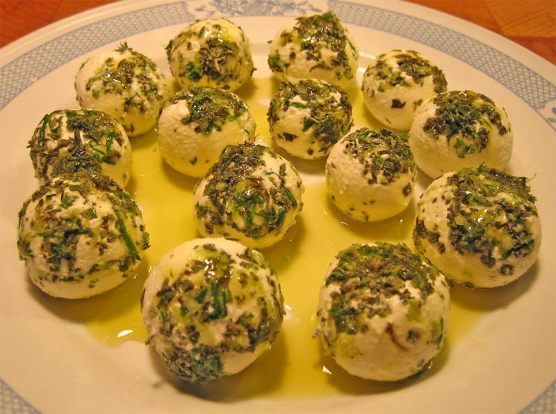 A plate with balls of soft white cheese set on it. The cheese has been rolled in herbs, and olive oil has been drizzled on top.