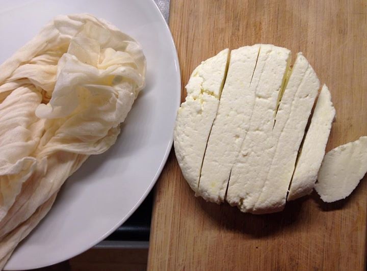 Homemade white cheese on a table, cut into pieces. The cheesecloth that was used to make the cheese in on a plate next to it.