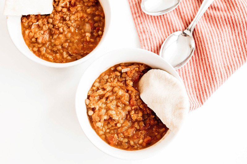 Two bowls of red lentil stew with pita bread on the side.
