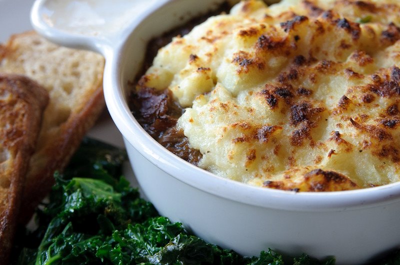 A baking dish filled with shepherd's pie. Leafy greens are on the side.